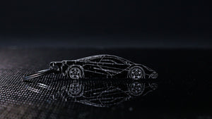 Carbon fiber McLaren F1 keychain displayed on a sheet of gloss carbon fiber